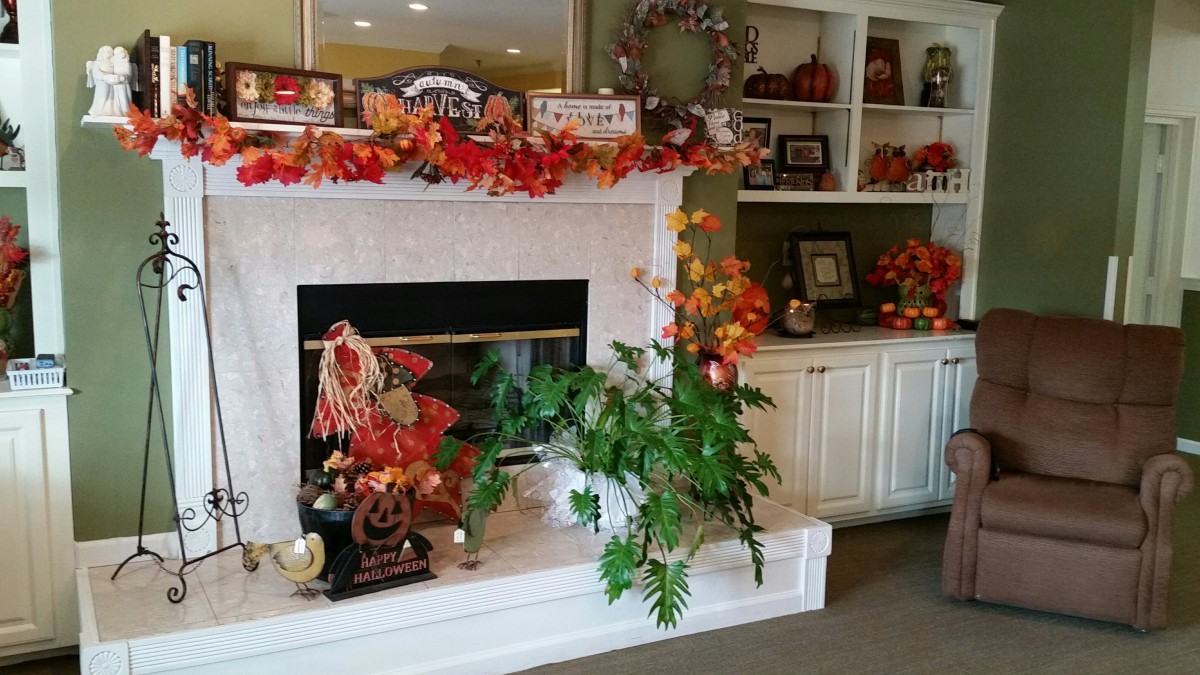 A cozy fireplace adorned with vibrant fall decorations, including leaves and pumpkins, creating a warm autumn atmosphere.
