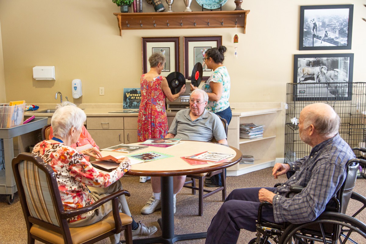Residents and staff interact in a community room at an assisted living facility.