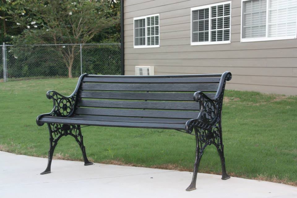 A black metal bench situated on a paved area near a building with windows.