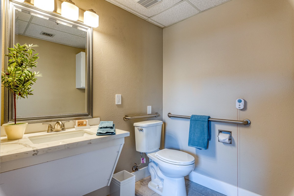 A clean and modern bathroom with a toilet, sink, mirror, and a blue towel hanging on the rack.