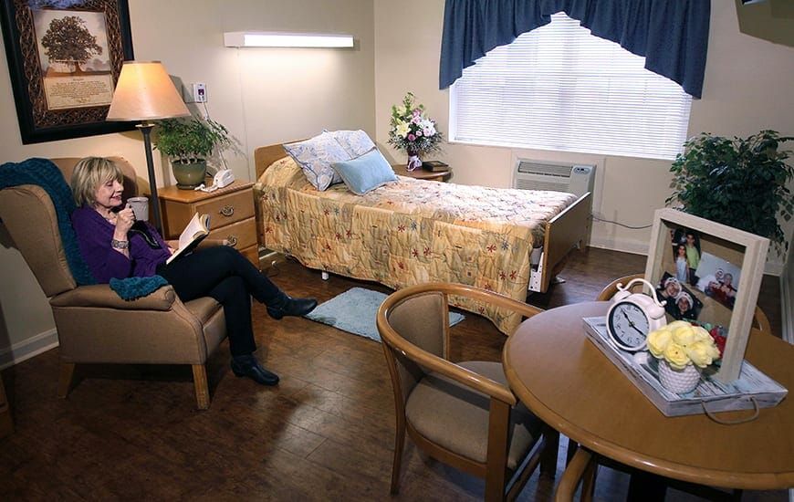 A hospital room with a bed, table, chair, and a person sitting.
