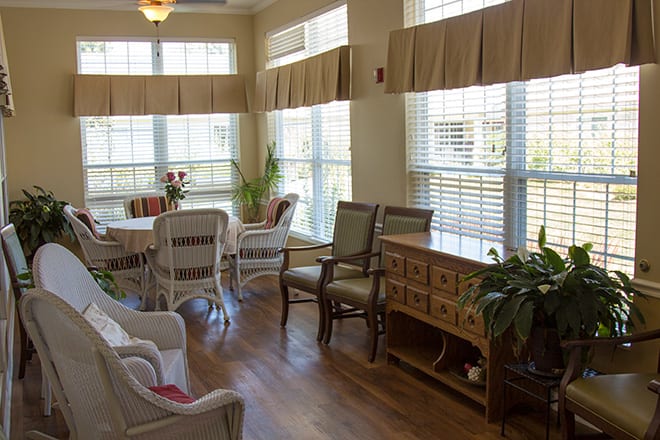 A bright sunroom with wicker furniture, dining table, large windows, and indoor plants.