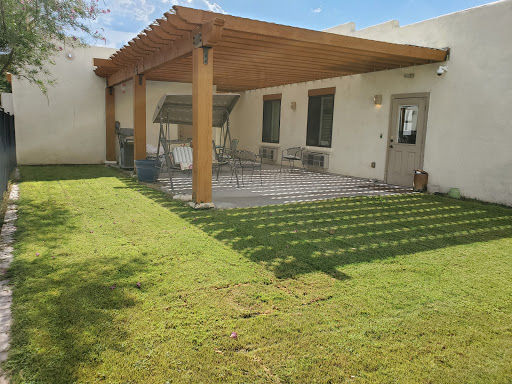 A cozy backyard featuring a shaded patio under a wooden pergola, surrounded by lush green grass.