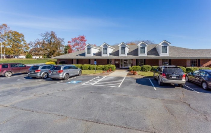 A parking lot in front of a single-story building with multiple cars parked under a clear blue sky.