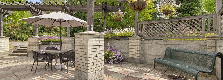 A serene patio area with brick pillars, hanging plants, and blooming flowers under a wooden pergola.