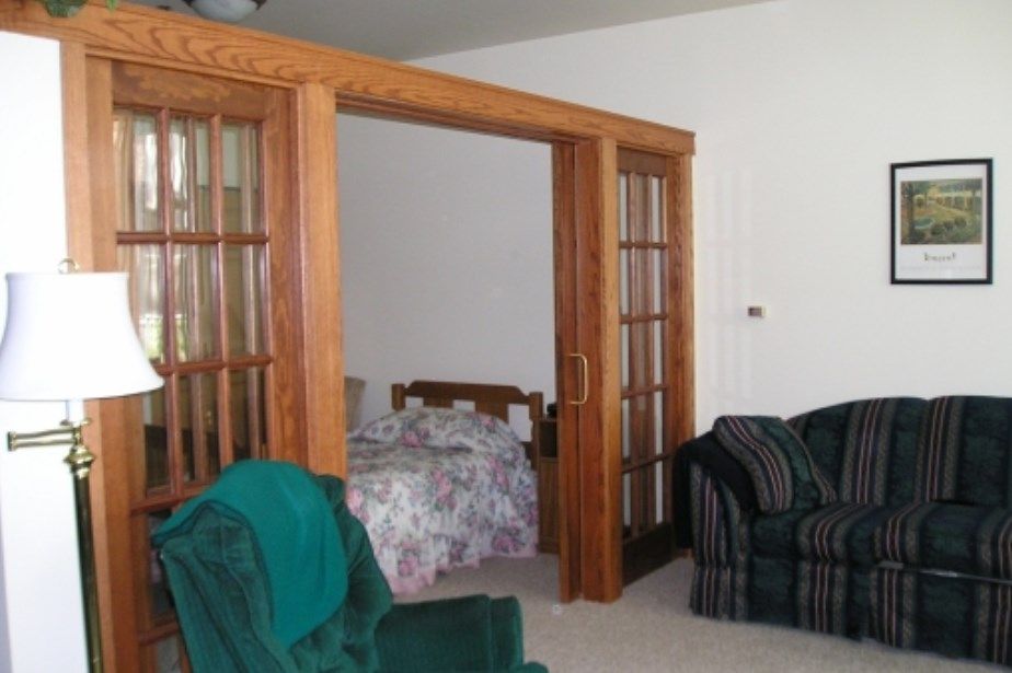 A cozy living room with wooden French doors leading to a bedroom, featuring comfortable seating and a bed.