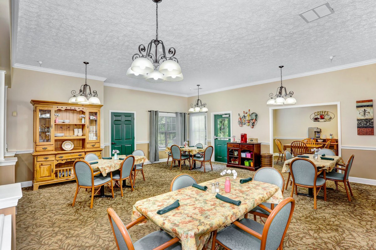 A well-decorated dining room with multiple tables and chairs, illuminated by elegant chandeliers.