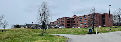 A view of a medical facility set against a cloudy sky, surrounded by grass and a leafless tree.