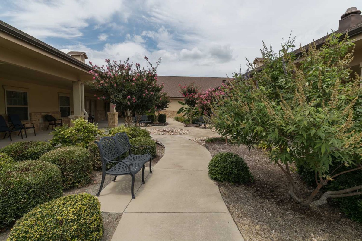 A serene garden path with benches and lush greenery on a cloudy day.