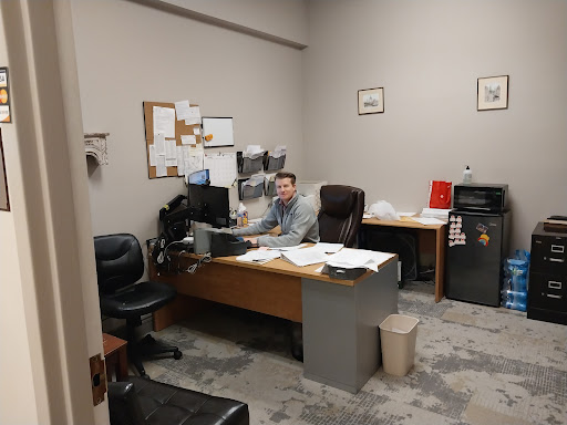 An office space featuring a desk, computer, and an individual working amidst documents.