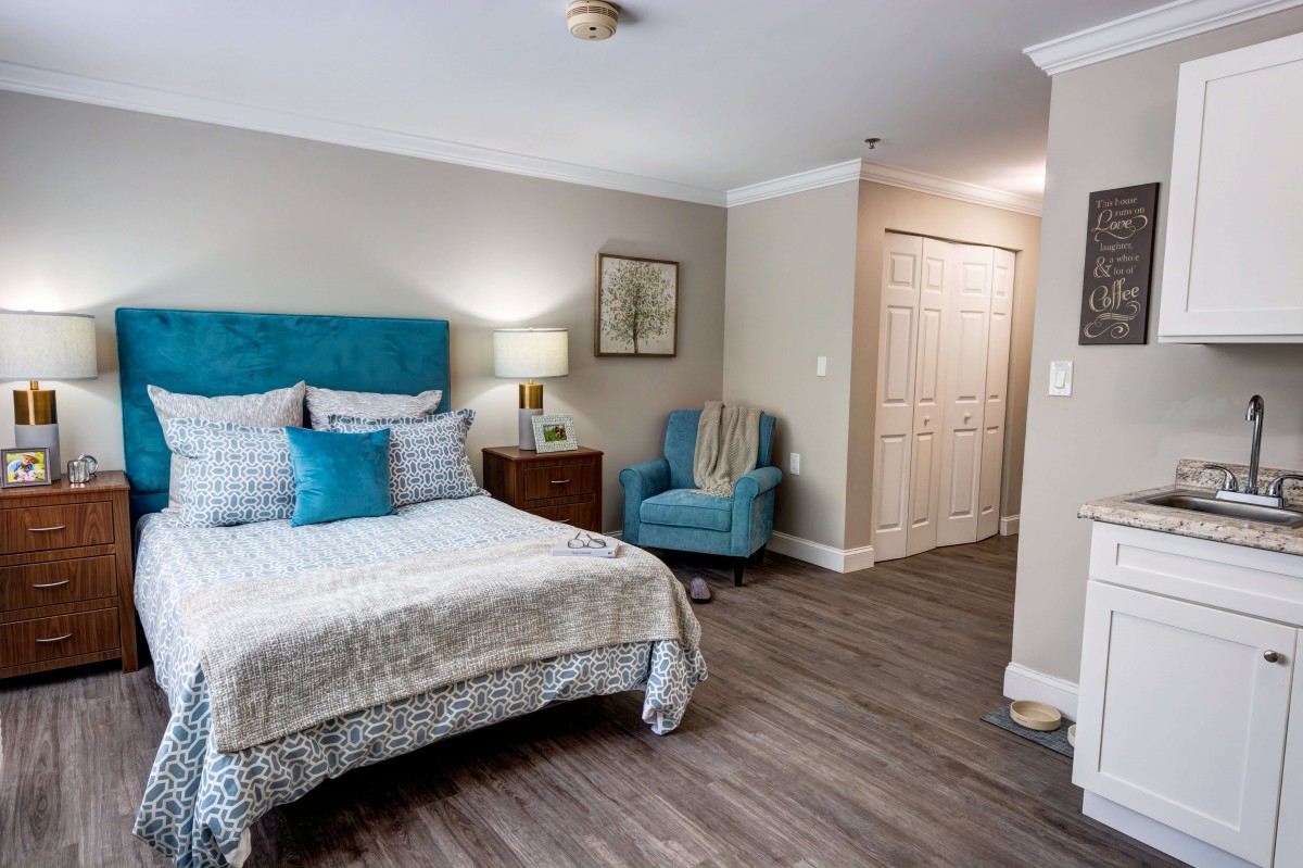 A cozy bedroom with modern decor, featuring a bed, armchair, lamp, and wood flooring.