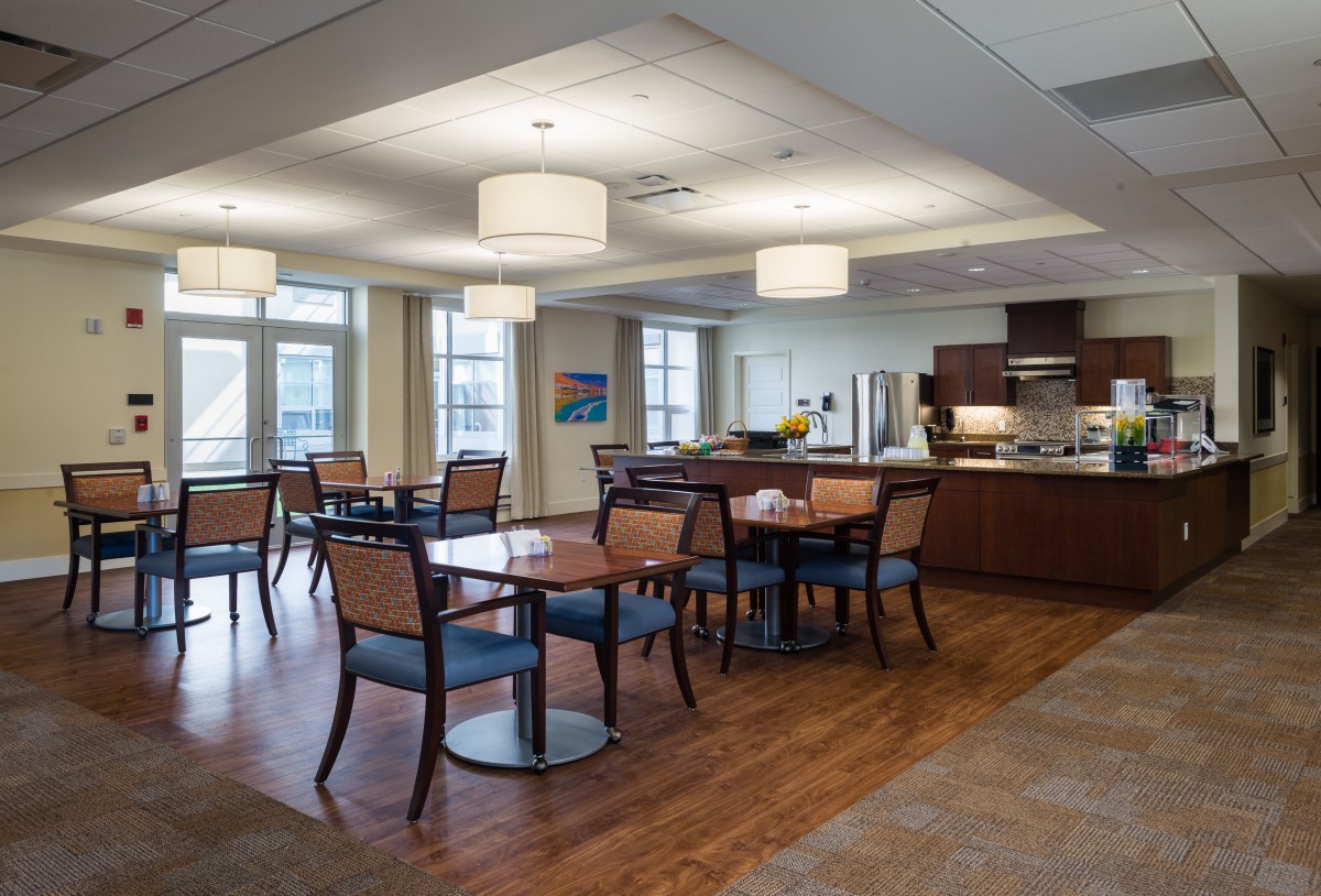 A modern dining area with tables and chairs, featuring a kitchen in the background and stylish light fixtures.
