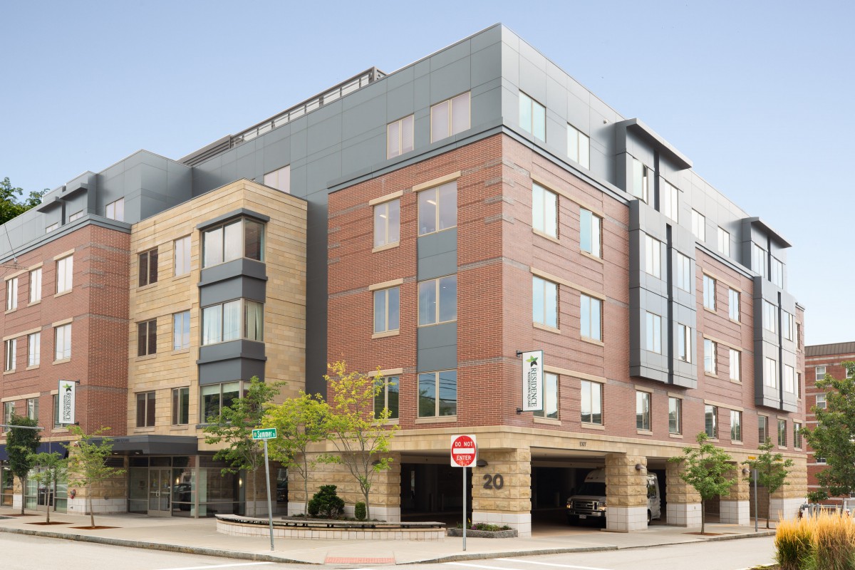 A modern apartment building with a blend of brick and glass exterior, located in an urban setting.