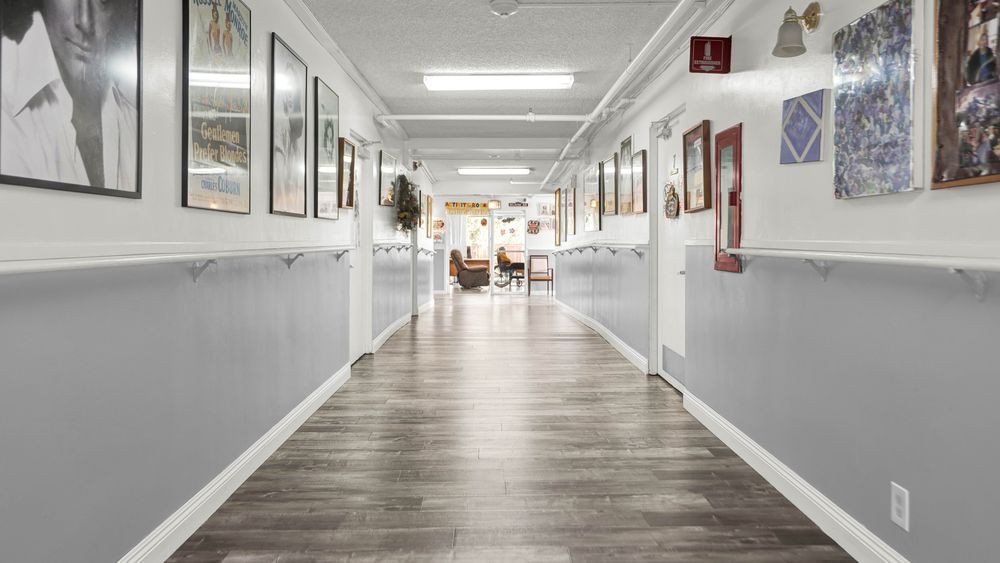 A well-lit hallway with wood flooring and framed pictures on the walls.