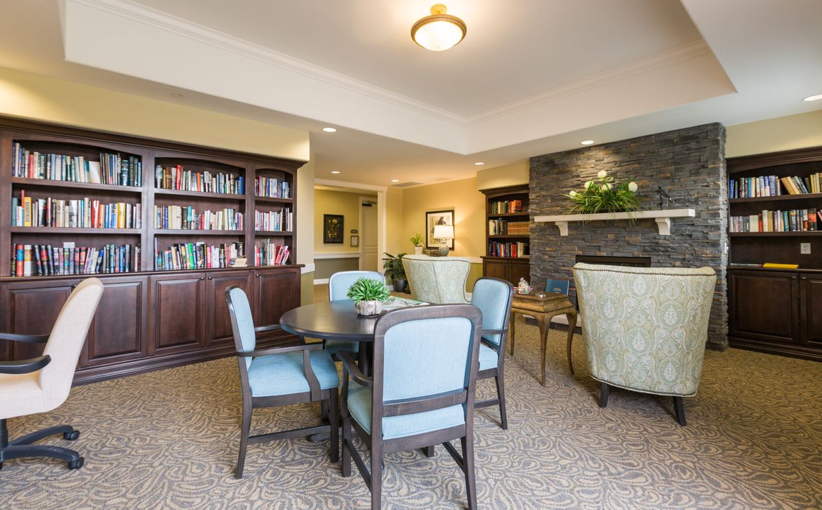 A cozy reading room featuring a bookshelf, table, and chairs under warm lighting.