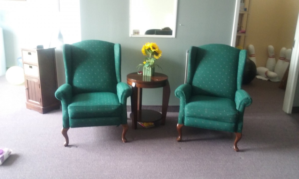 Two green armchairs flank a small table with a vase of sunflowers in a cozy living room setting.