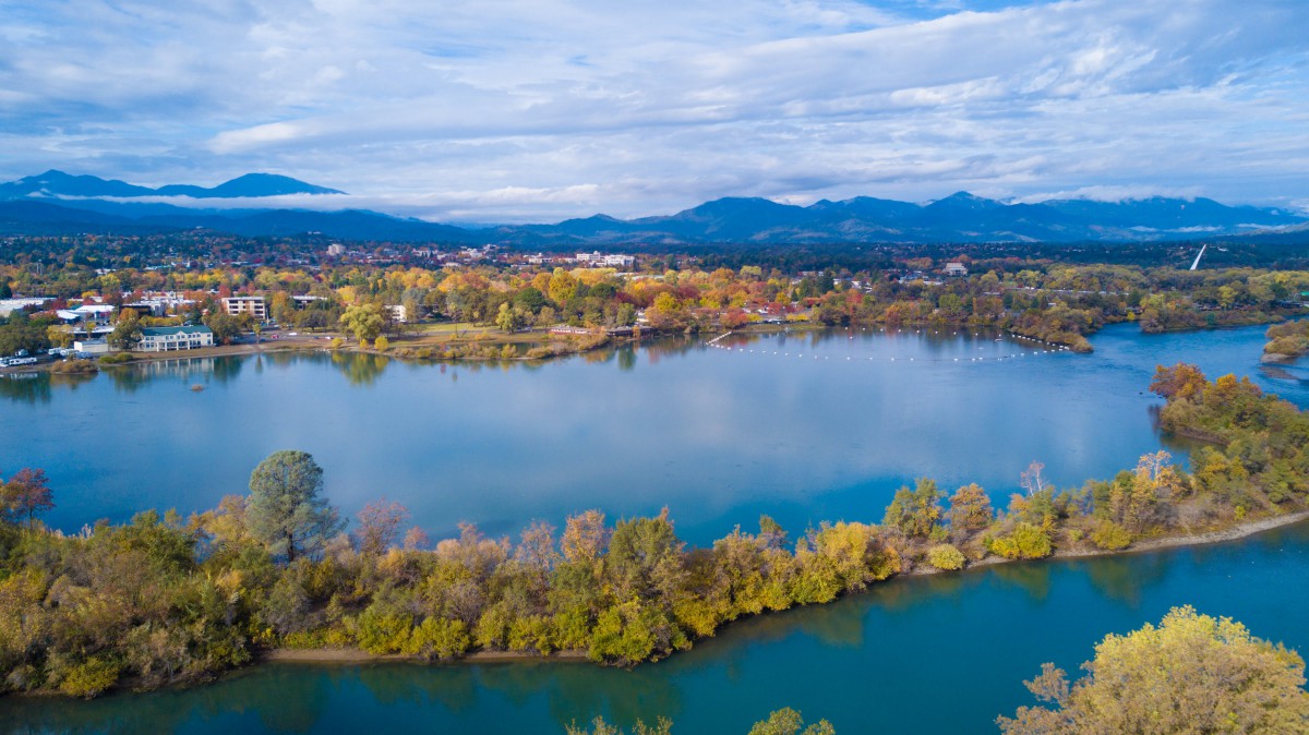 A scenic view of a lake surrounded by autumn foliage with mountains in the background.