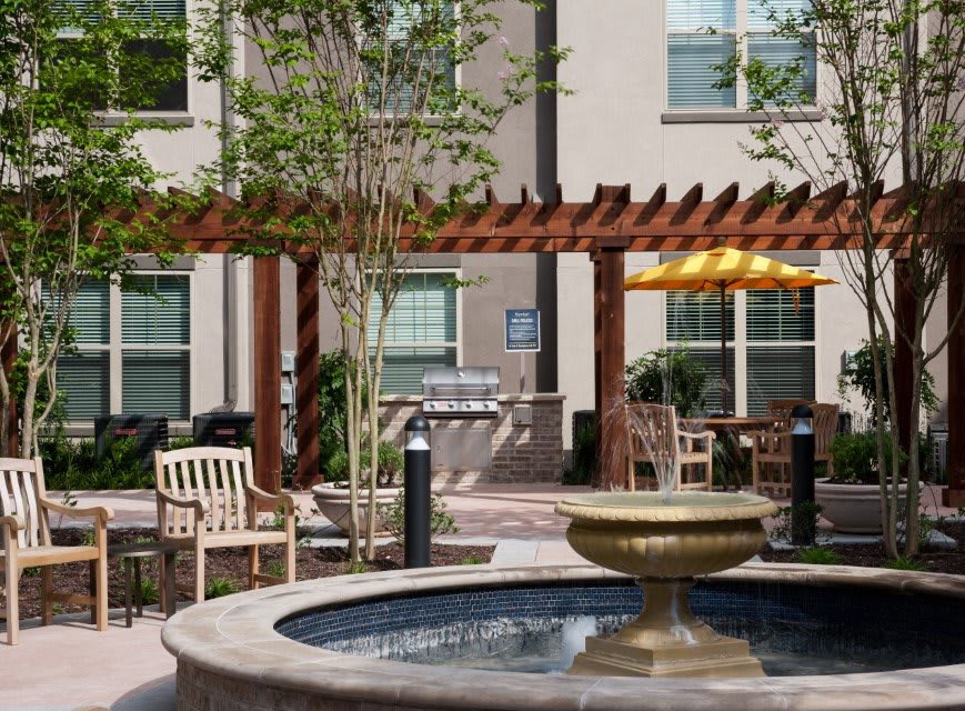 A peaceful courtyard with a central fountain, surrounded by outdoor seating and a wooden pergola.