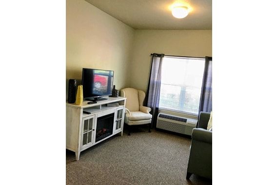 A cozy living room with a television, chair, and large window.
