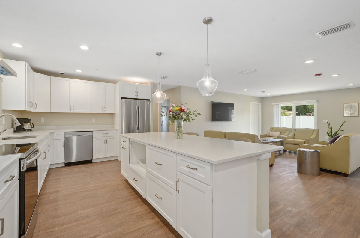 A modern kitchen with white cabinetry and a large central island, featuring pendant lights and stainless steel appliances.
