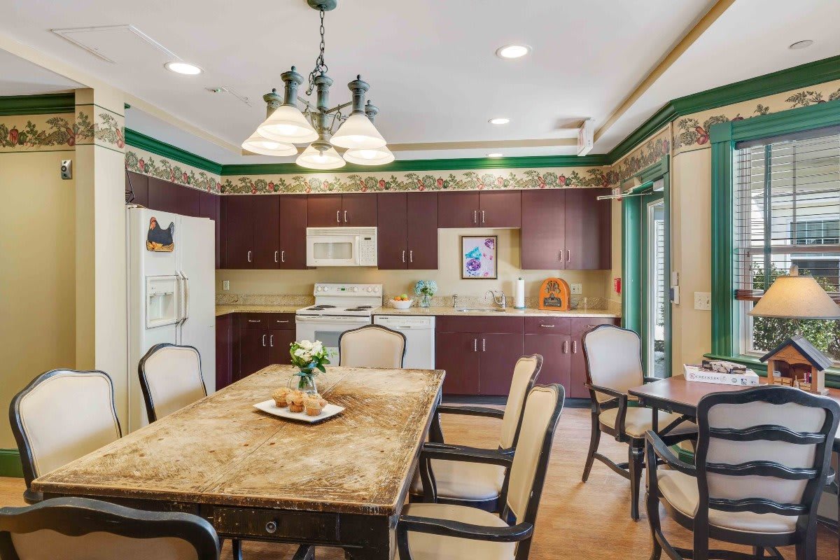 A cozy kitchen and dining area with a large table, chairs, wooden cabinets, and decorative lighting.