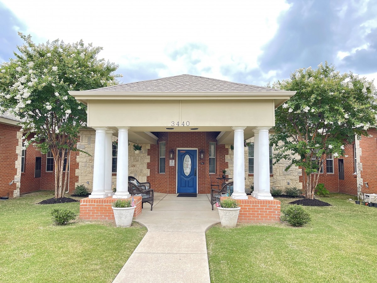 A charming house entrance with columns, a blue door, and landscaped front yard.