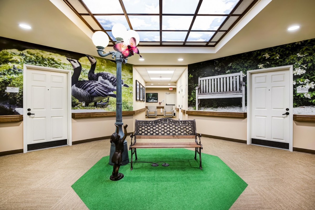 An indoor hallway featuring a bench on artificial grass, flanked by decorative murals and a lamp post.
