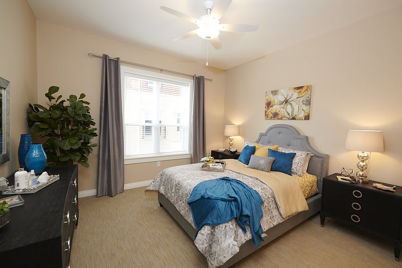A cozy bedroom with stylish decor featuring a neatly made bed, curtains framing a large window, and a small lamp adding warmth to the room.