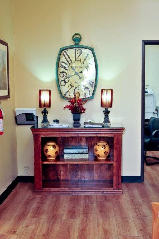 A neatly decorated interior space featuring a wooden shelf, two lamps, decorative vases, and a large wall clock.