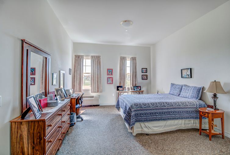 A spacious bedroom with a neatly made bed, multiple windows, and a wooden dresser.