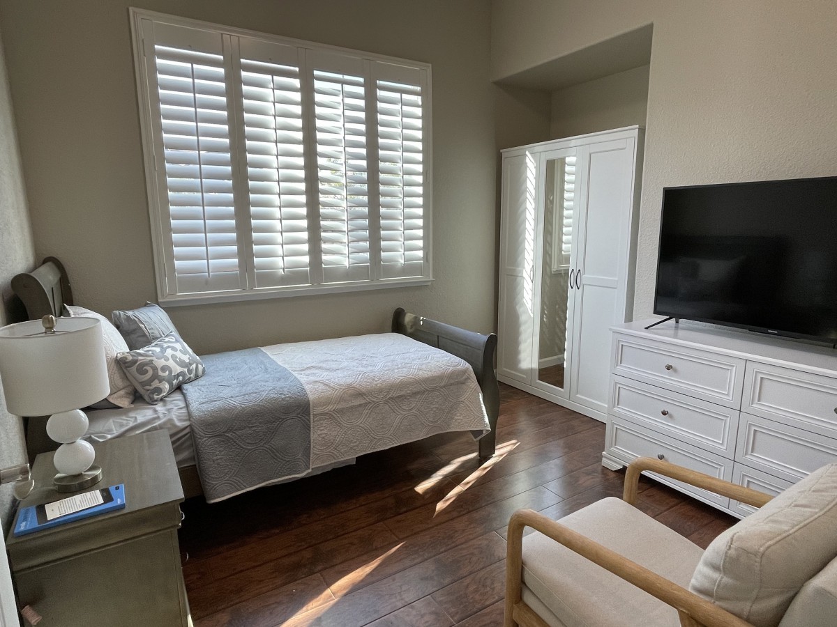 A bright and cozy bedroom with modern furnishings, including a bed, mirror, and TV.