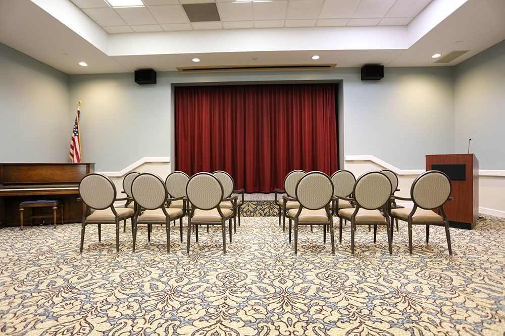 A small conference room with rows of chairs facing a red curtain.