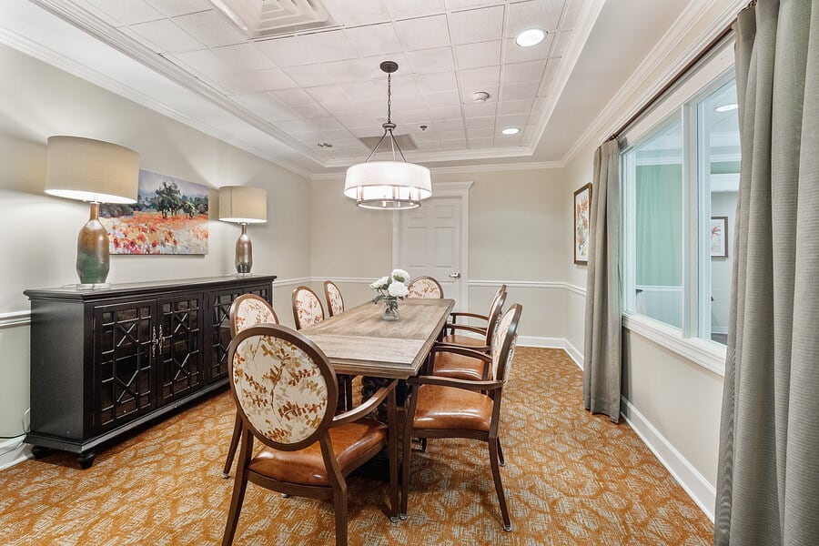 A well-appointed dining or conference room with a central wooden table, surrounded by upholstered chairs, featuring a chandelier above and artwork on the walls.