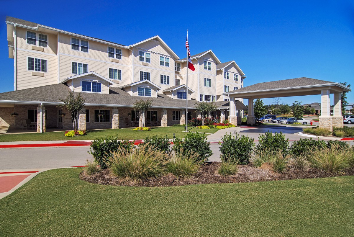 A large residential building surrounded by well-maintained landscaping under a clear blue sky.