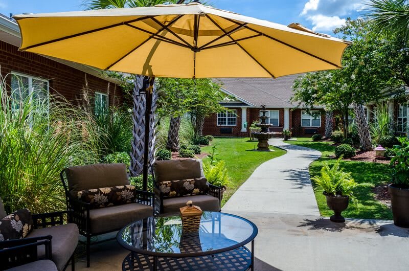 A sunny outdoor patio with comfortable seating and a large yellow umbrella in a well-maintained garden.