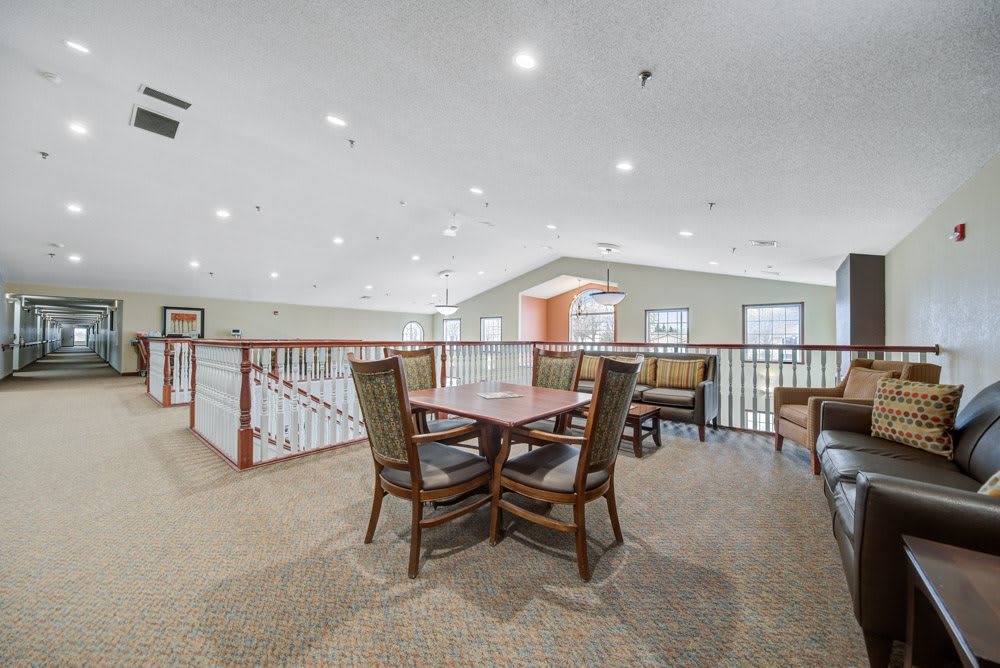 A spacious indoor seating area with a table and chairs, featuring carpeted flooring and ceiling lighting.