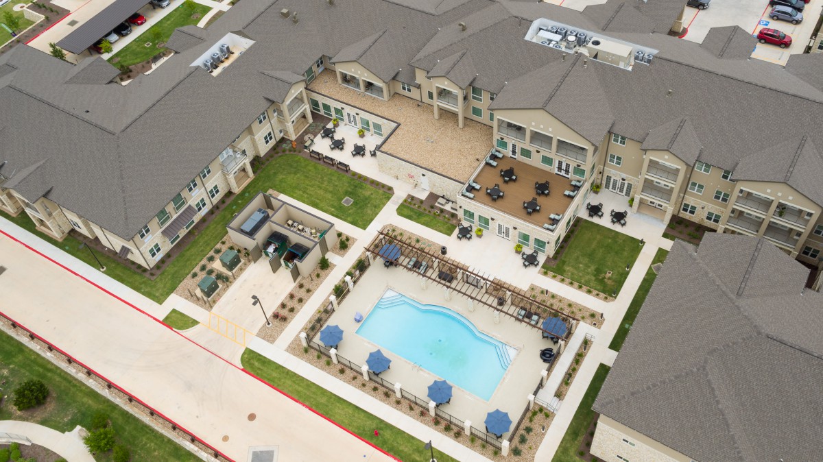 Aerial view of an apartment complex featuring a central swimming pool and outdoor seating area.