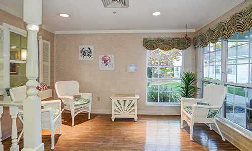 A cozy waiting room with white chairs, a small table, wall art, and plants by the window.