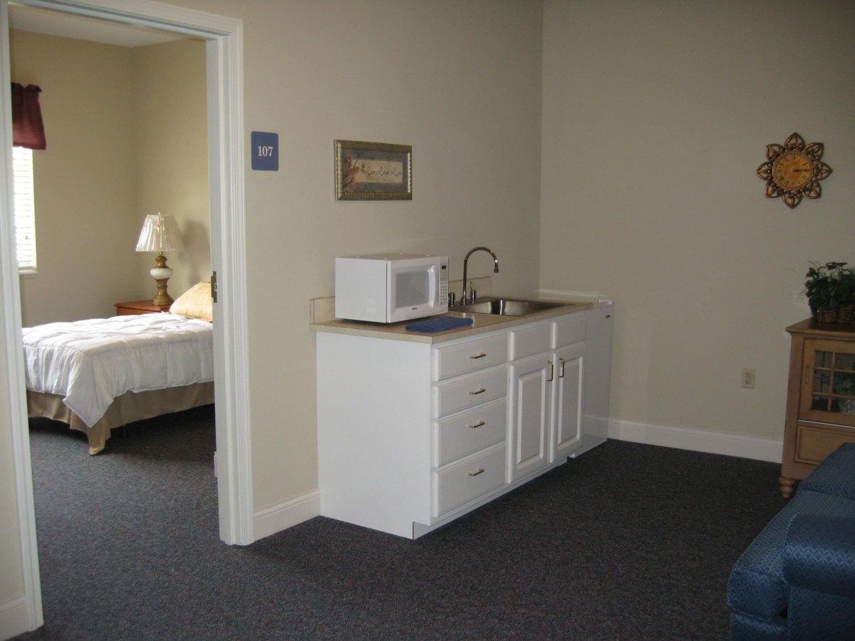A small kitchenette area with a microwave and sink adjacent to a bedroom.