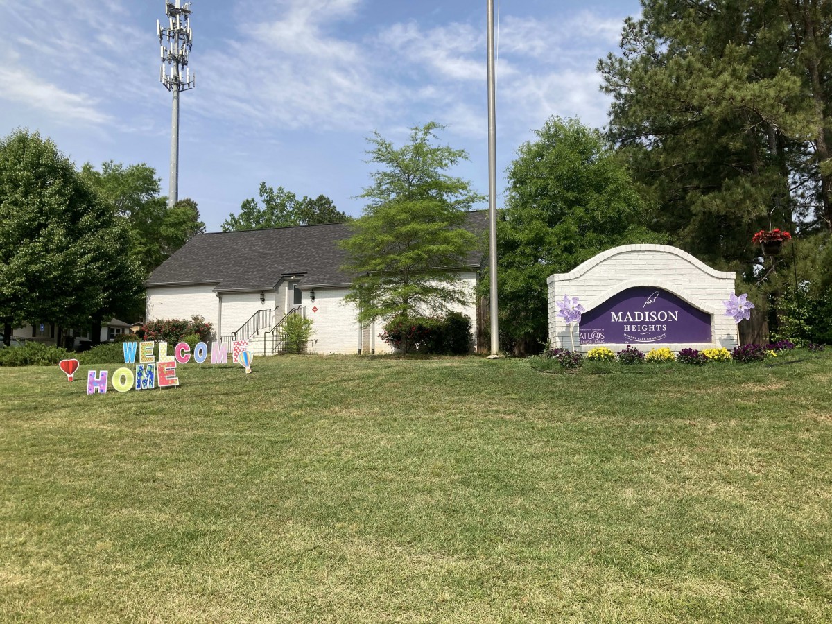 A small building with a welcome sign on a grassy area surrounded by trees.
