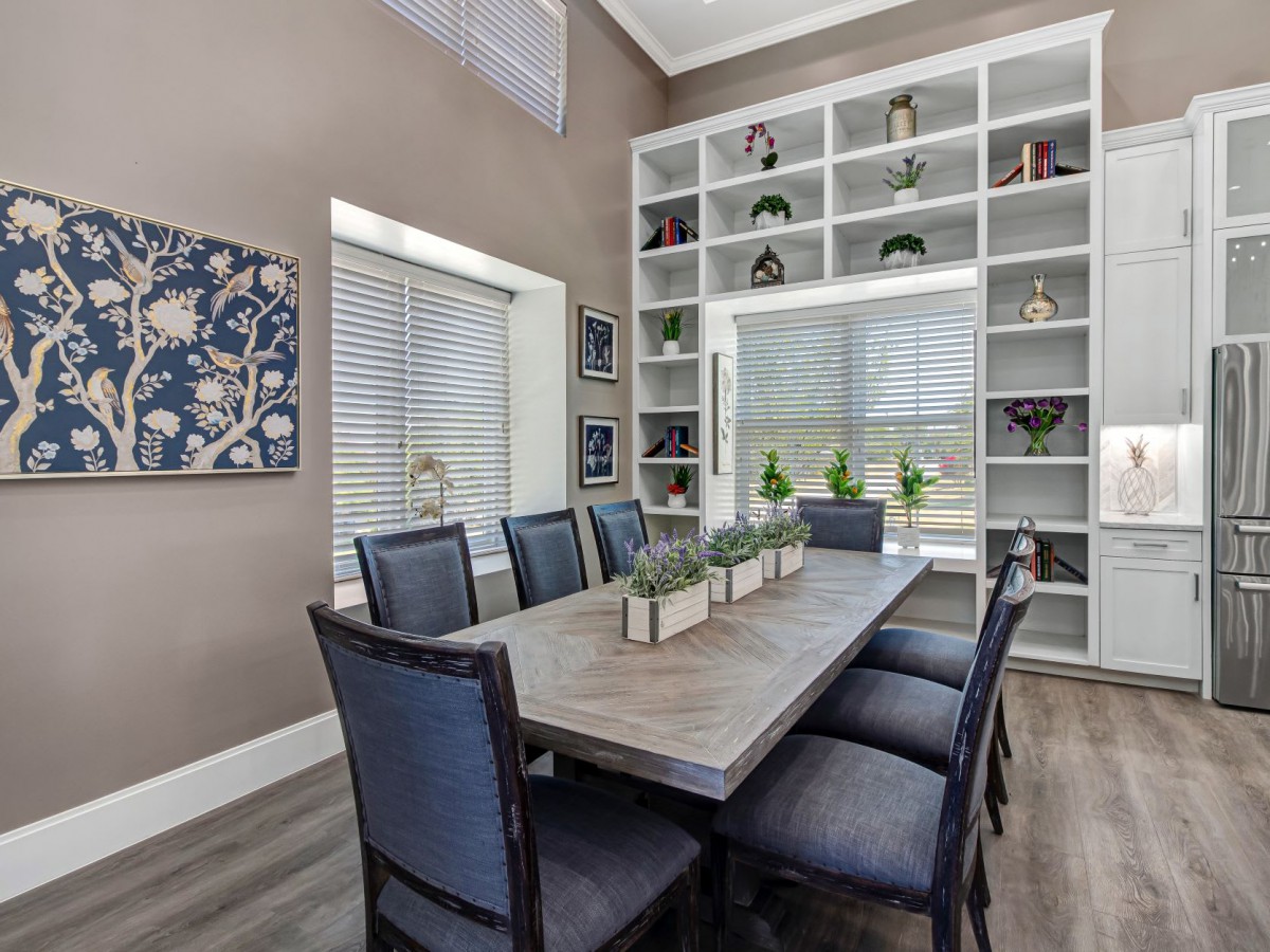 A modern dining room with a large table and chairs, surrounded by shelves filled with decorative items and plants.