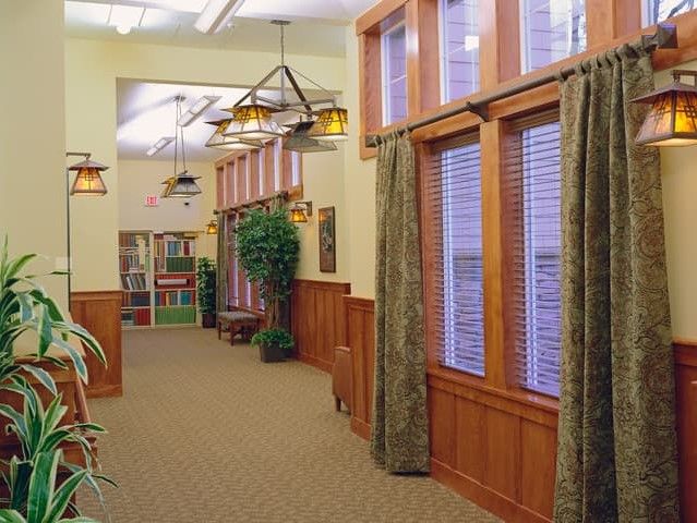 A well-lit hallway with wooden paneling, large windows, and decorative plants.