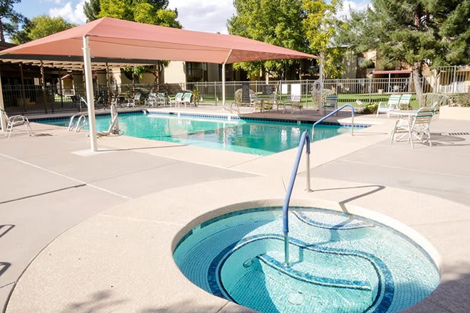 An outdoor swimming pool area with a jacuzzi and sunshade, surrounded by trees.