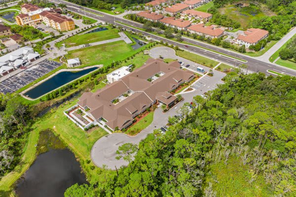 Aerial view of a building complex surrounded by roads, greenery, and a water body.