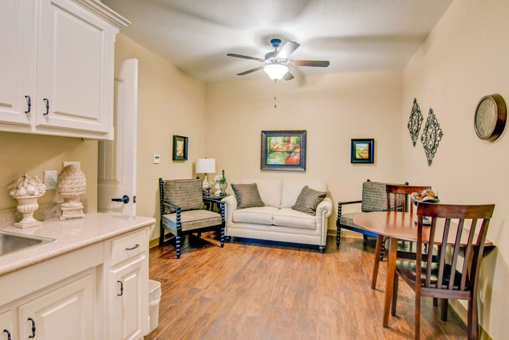 A cozy living room with a sofa, chairs, and a small dining area, featuring wooden flooring and decorative artwork.