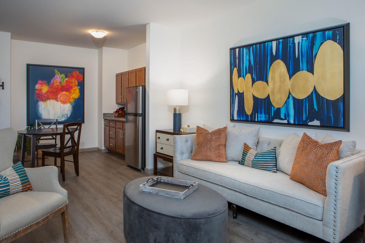 A modern living room with colorful artwork and a view into the kitchen area.