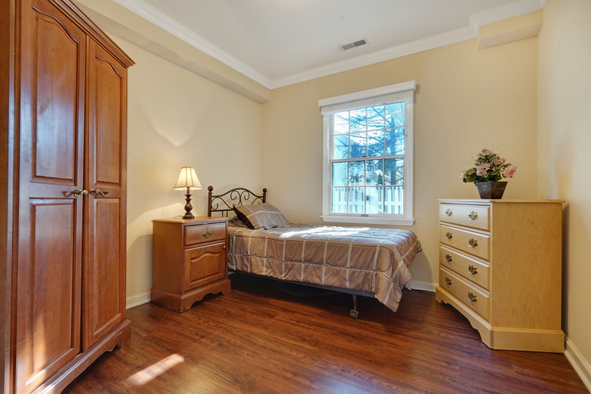A cozy bedroom with a single bed, wooden furniture, and a window letting in natural light.