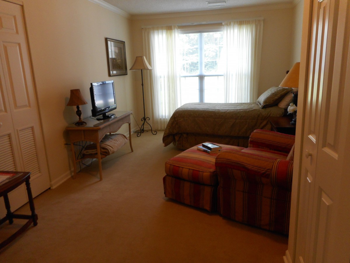 A cozy bedroom with a bed, TV, and armchair near a window.