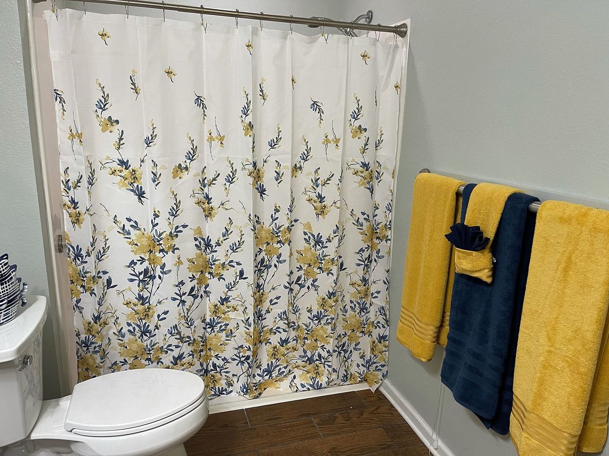 A bathroom featuring a floral-patterned shower curtain and neatly arranged yellow and blue towels.