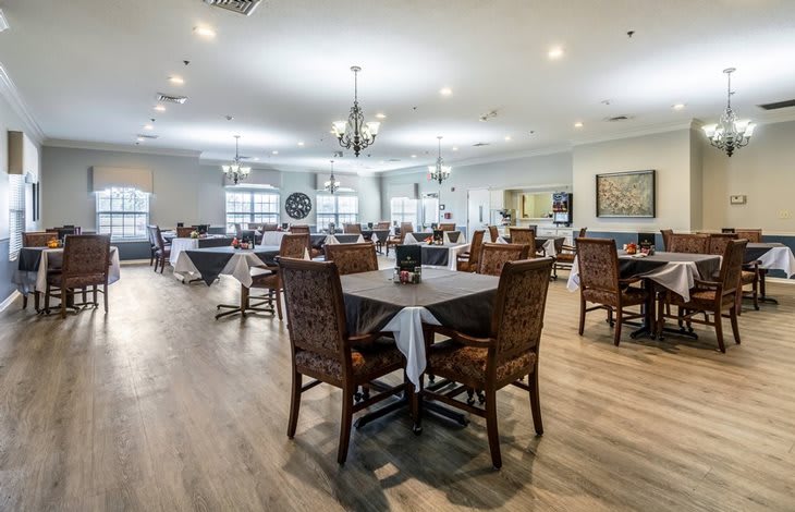 A spacious dining room with neatly arranged tables and chairs, adorned with chandeliers and wooden flooring.